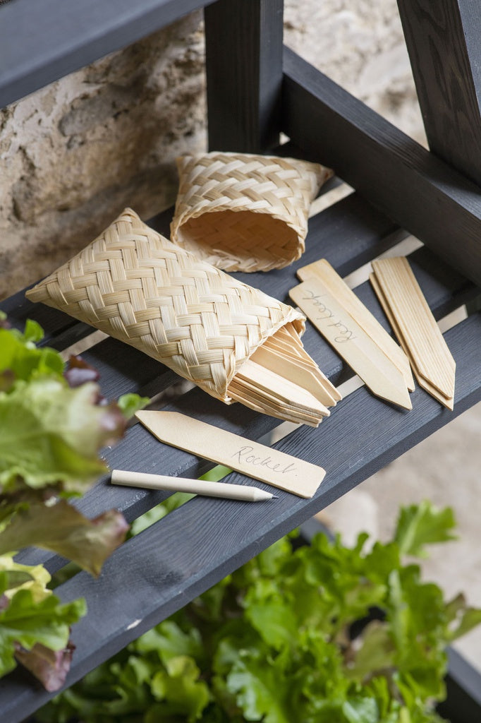 Woven plant labels on a wooden surface with plants in the foreground