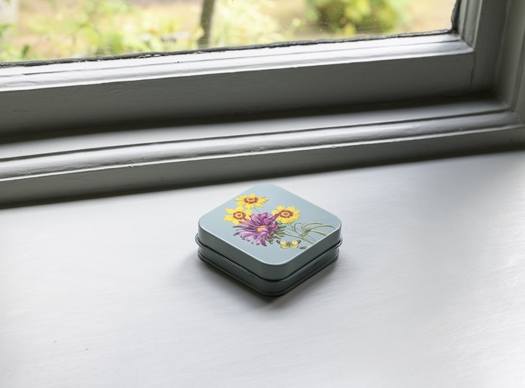 Small rectangular tin with floral design on a windowsill