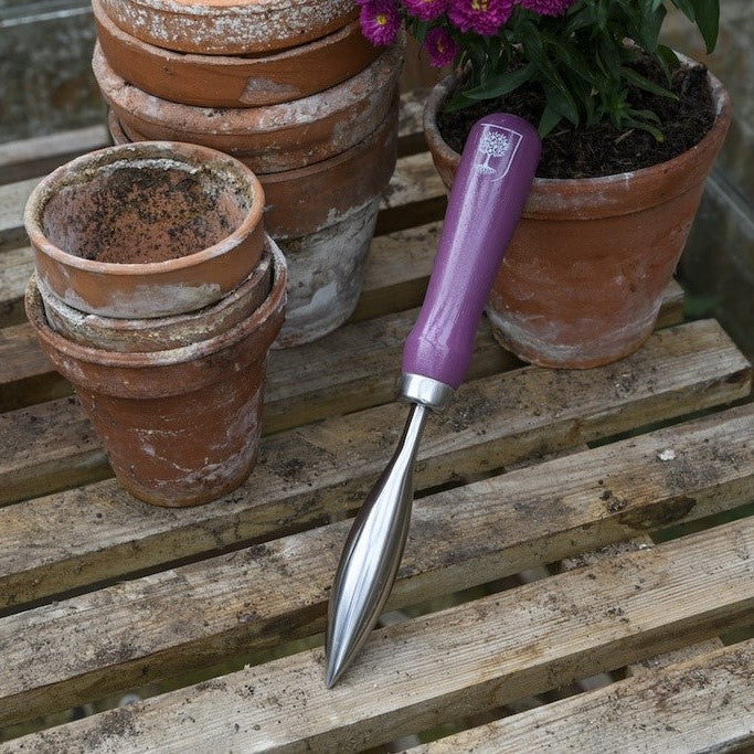 Gardening tool with purple handle on a wooden surface with potted plants.