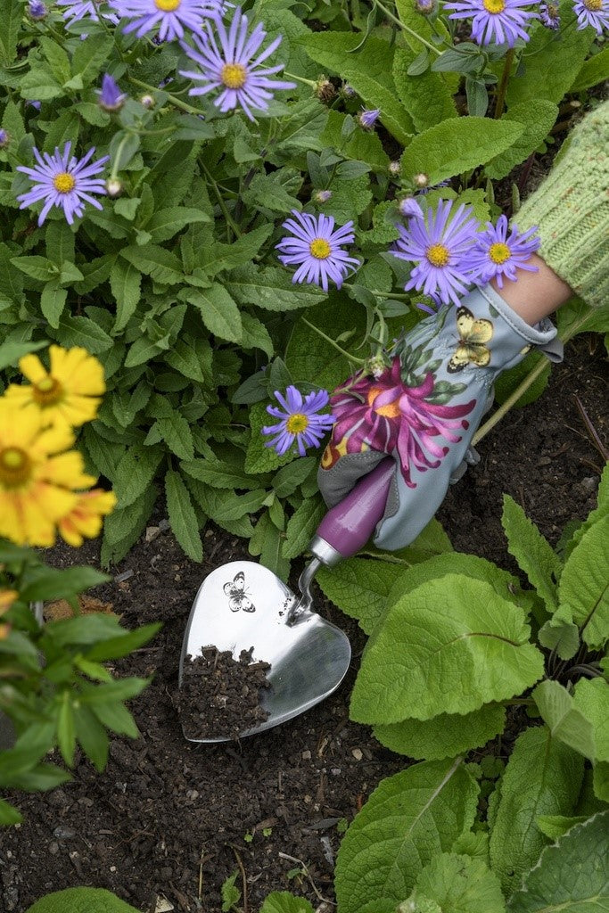 Gardening scene with a hand wearing a glove holding a small plant, surrounded by flowers and soil.