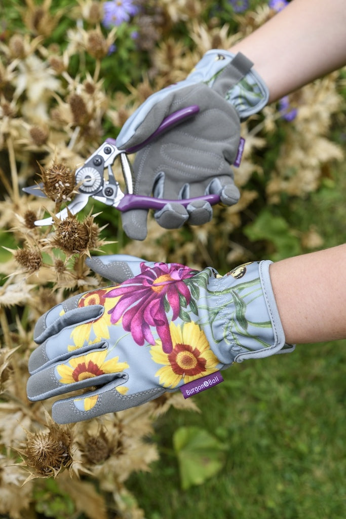 Gardening gloves with floral design holding a pair of pliers against a garden background