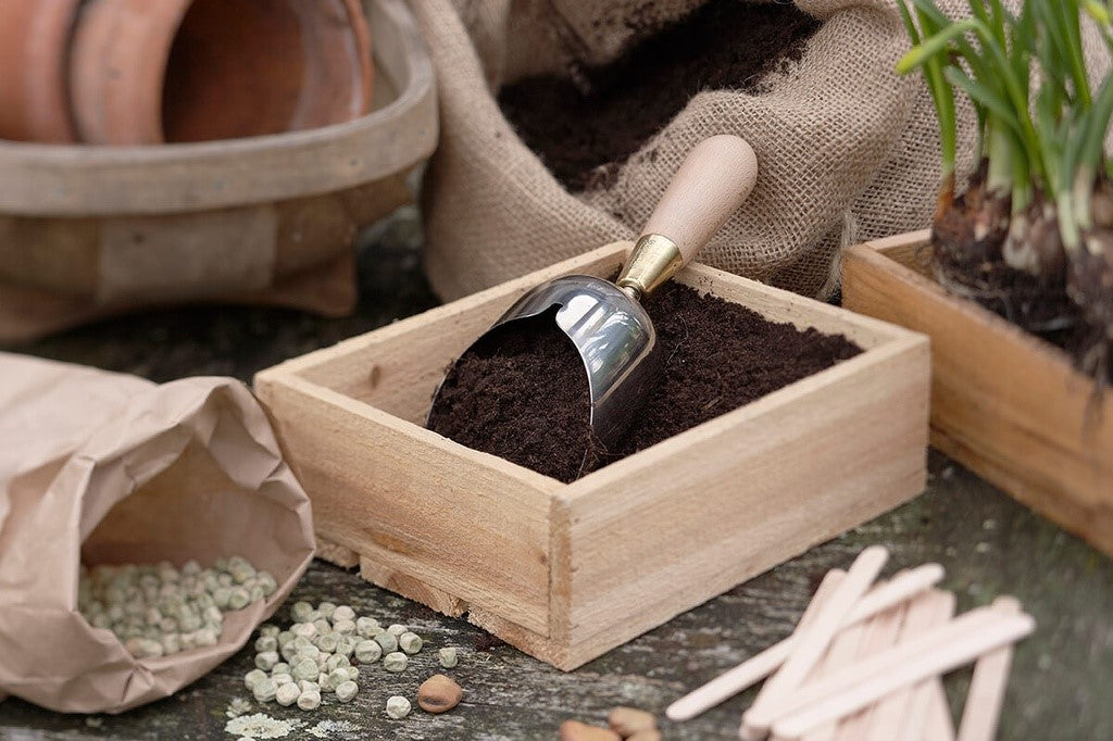 Wooden box with soil and a small scoop, surrounded by gardening tools and materials.