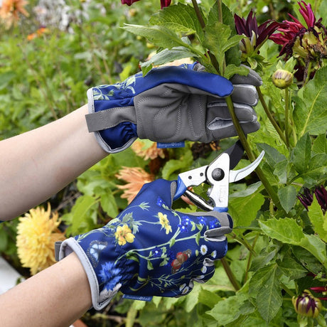 Person pruning flowers with gardening shears and gloves in a garden setting