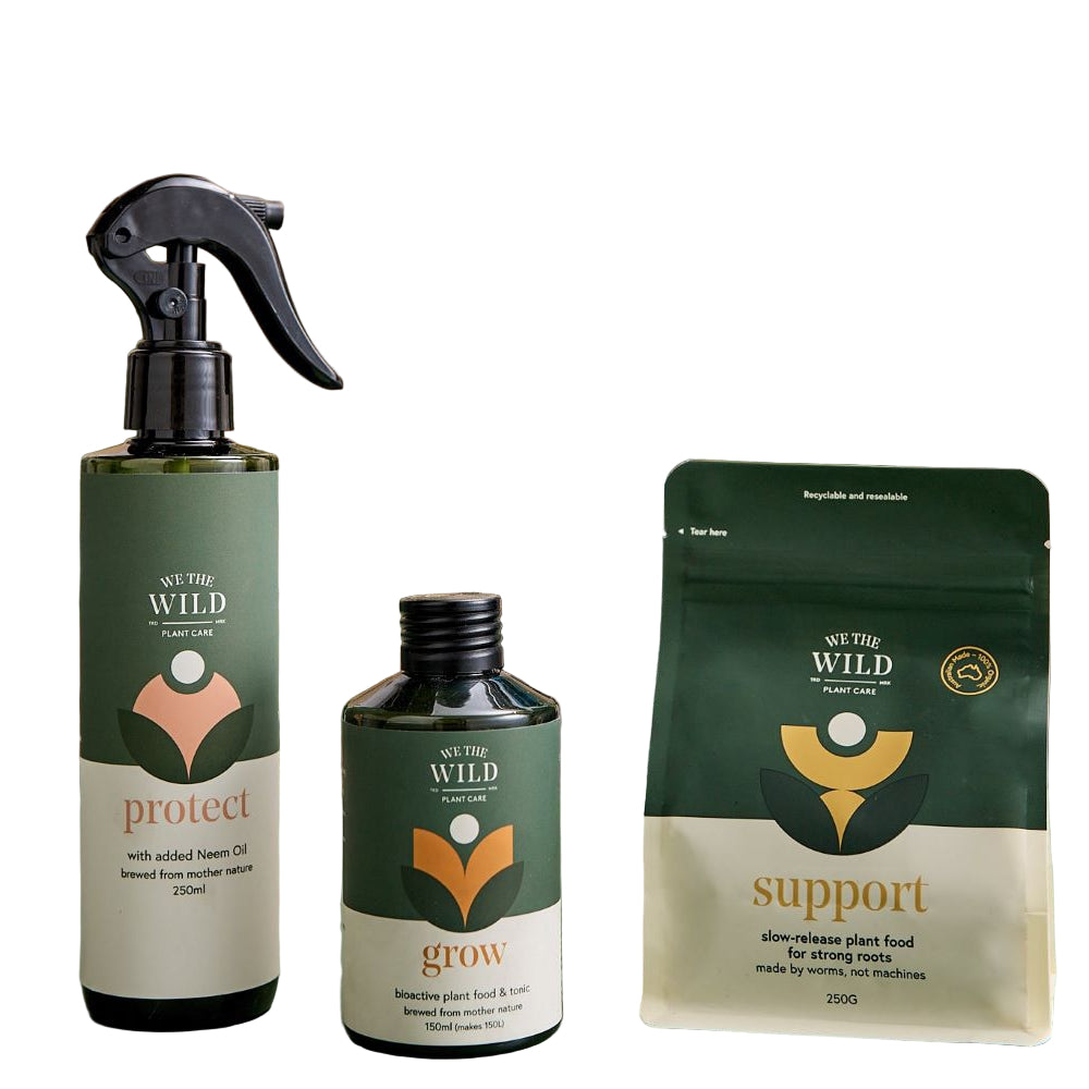 Three green bottles of plant food with labels on a table with plants on white background