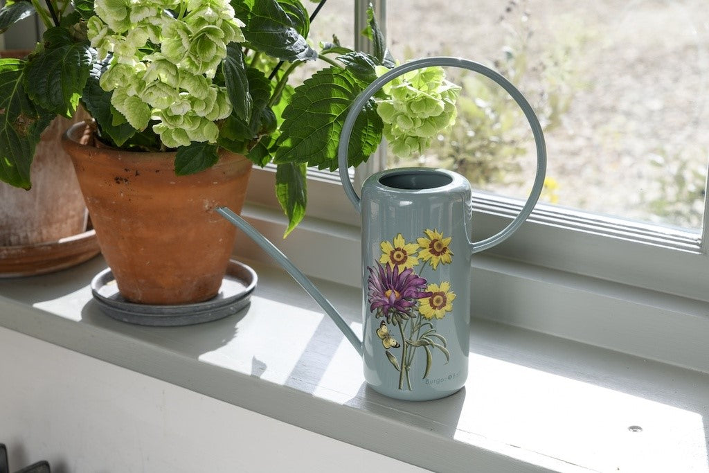 Decorative watering can with floral design on a windowsill next to potted plants