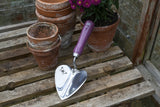Gardening trowel with purple handle on a wooden surface with potted plants.